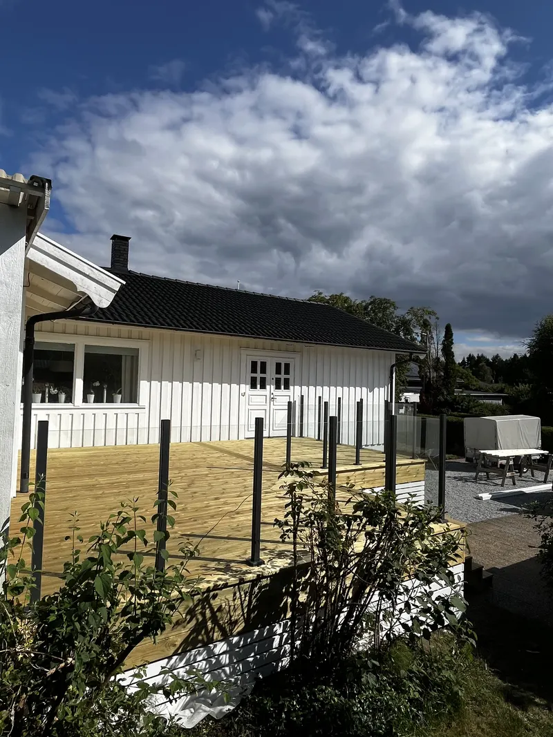 Stor träaltan med glasräcke och svarta stolpar sett från sidan