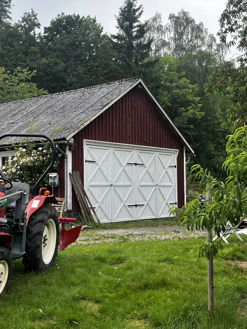 Röd lada med vita korsportar och gammal traktor framför